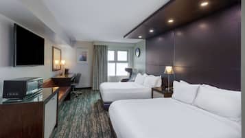 Habitación de hotel con dos camas, un escritorio, televisión, microondas, un reloj y una ventana con cortinas.