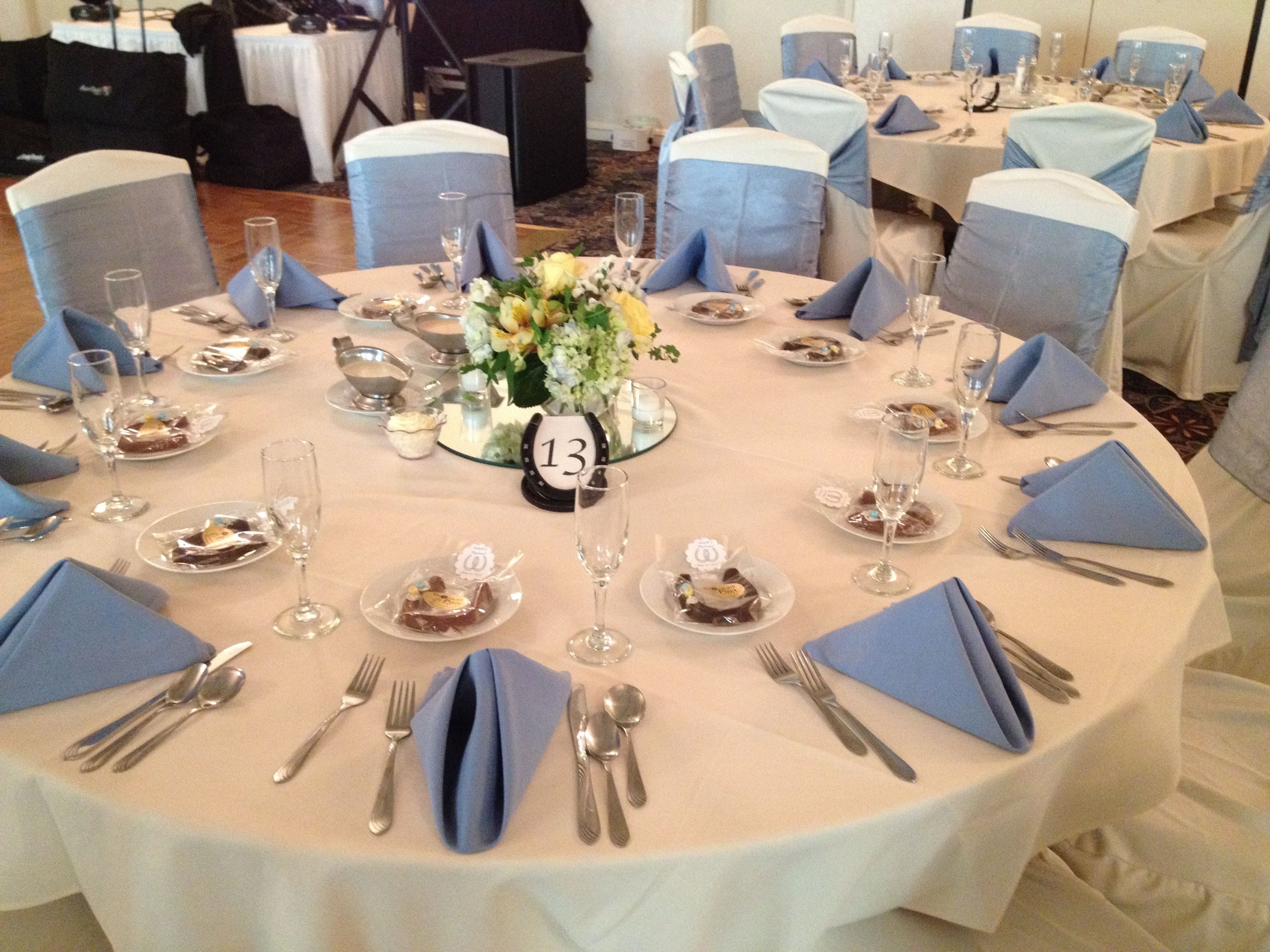 A round table set for a formal event with numbered place settings, blue napkins, and a floral centerpiece.