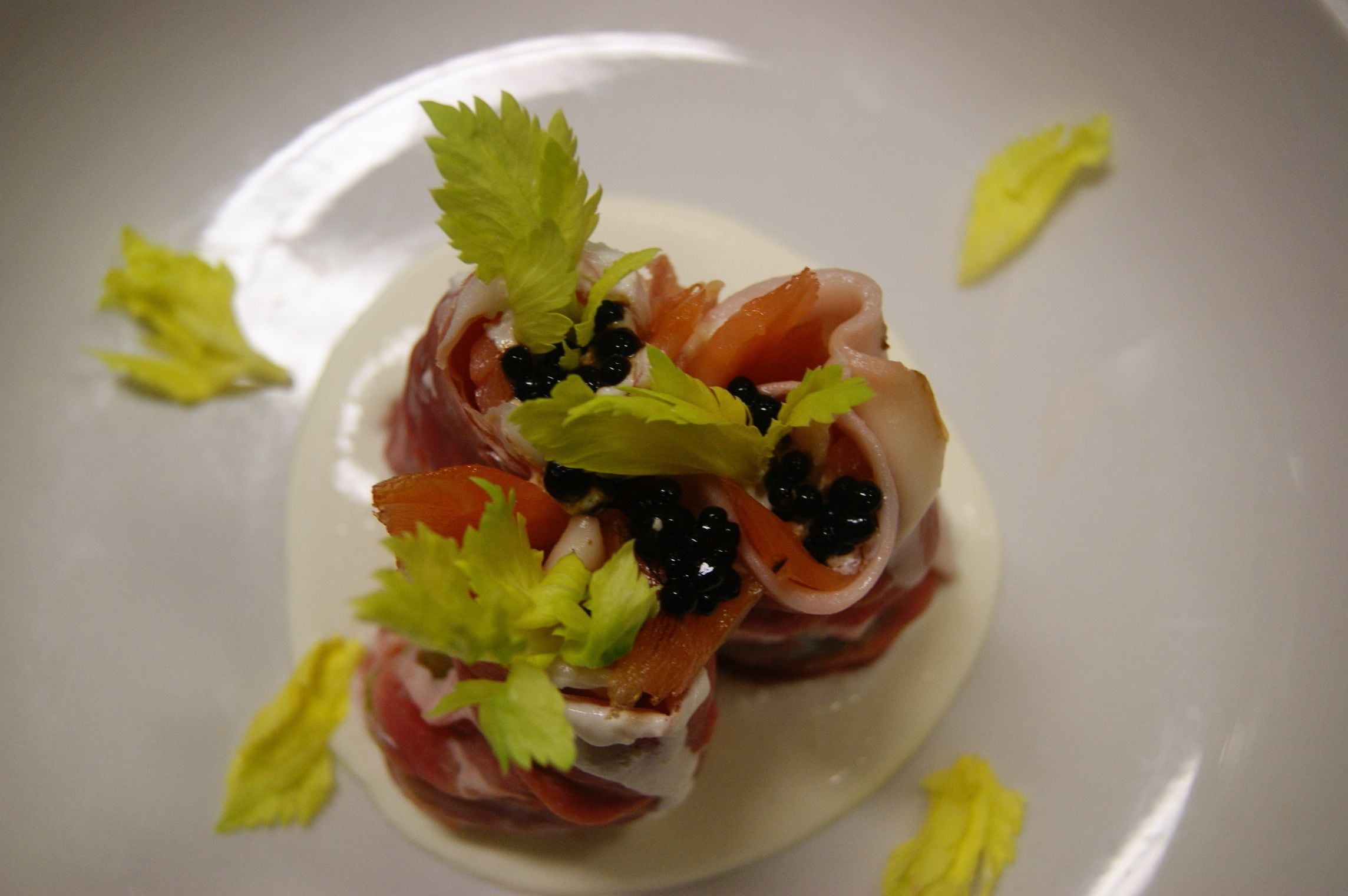 A plate with a dish of prosciutto, black caviar, and garnished with parsley.