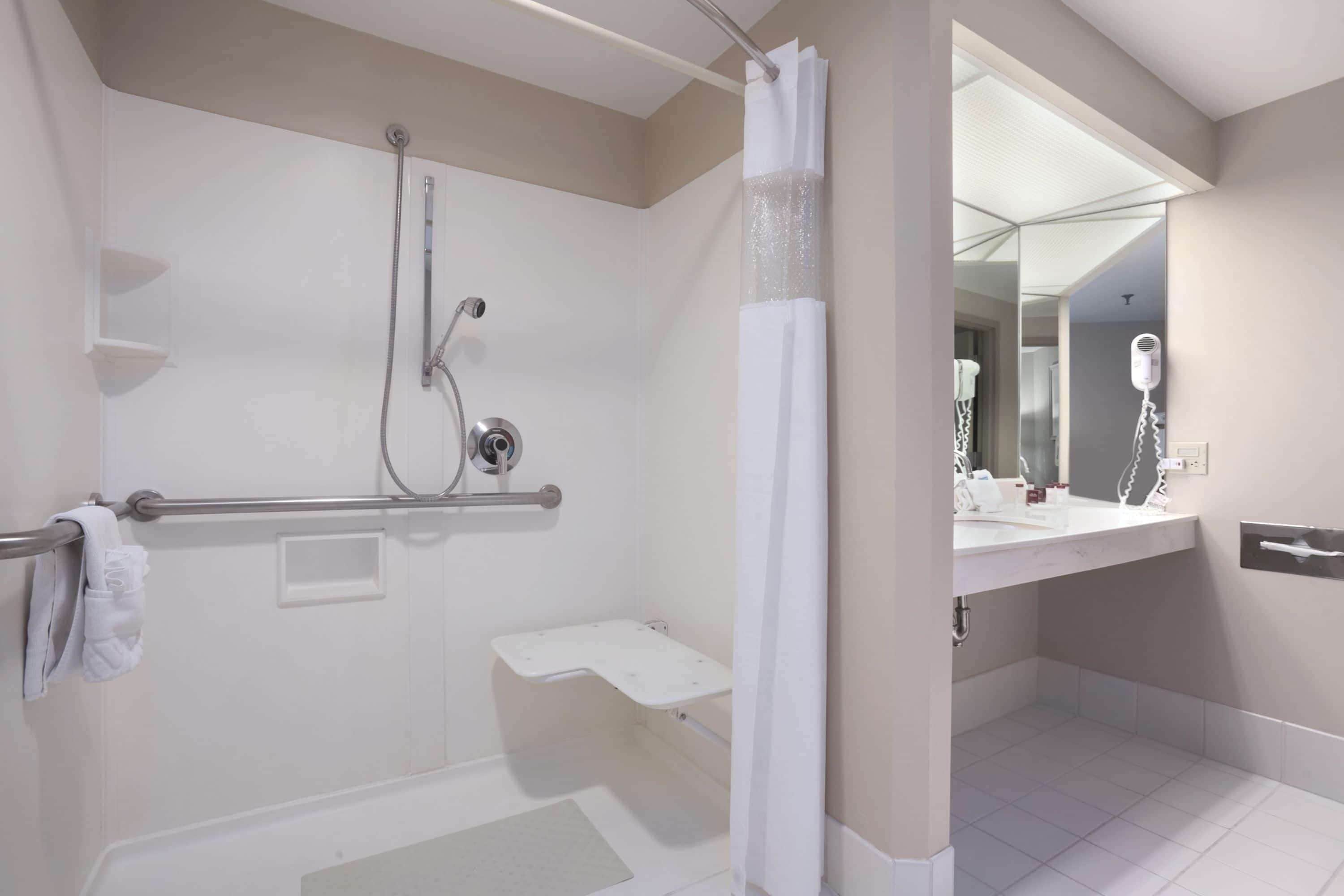 Une salle de bain moderne équipée d’une douche, d’un meuble-lavabo avec miroir et d’un sèche-cheveux.