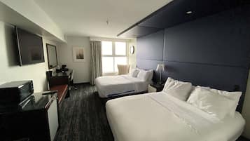 A hotel room with two beds, a desk with a TV, a clock, and a window with curtains.
