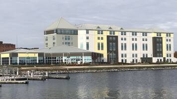 Un hotel frente al agua con un área de estar al aire libre techada, un muelle con aves y un edificio grande con múltiples ventanas.