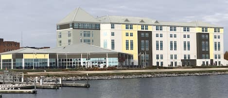 Un hotel frente al agua con un área de estar al aire libre techada, un muelle con aves y un edificio grande con múltiples ventanas.