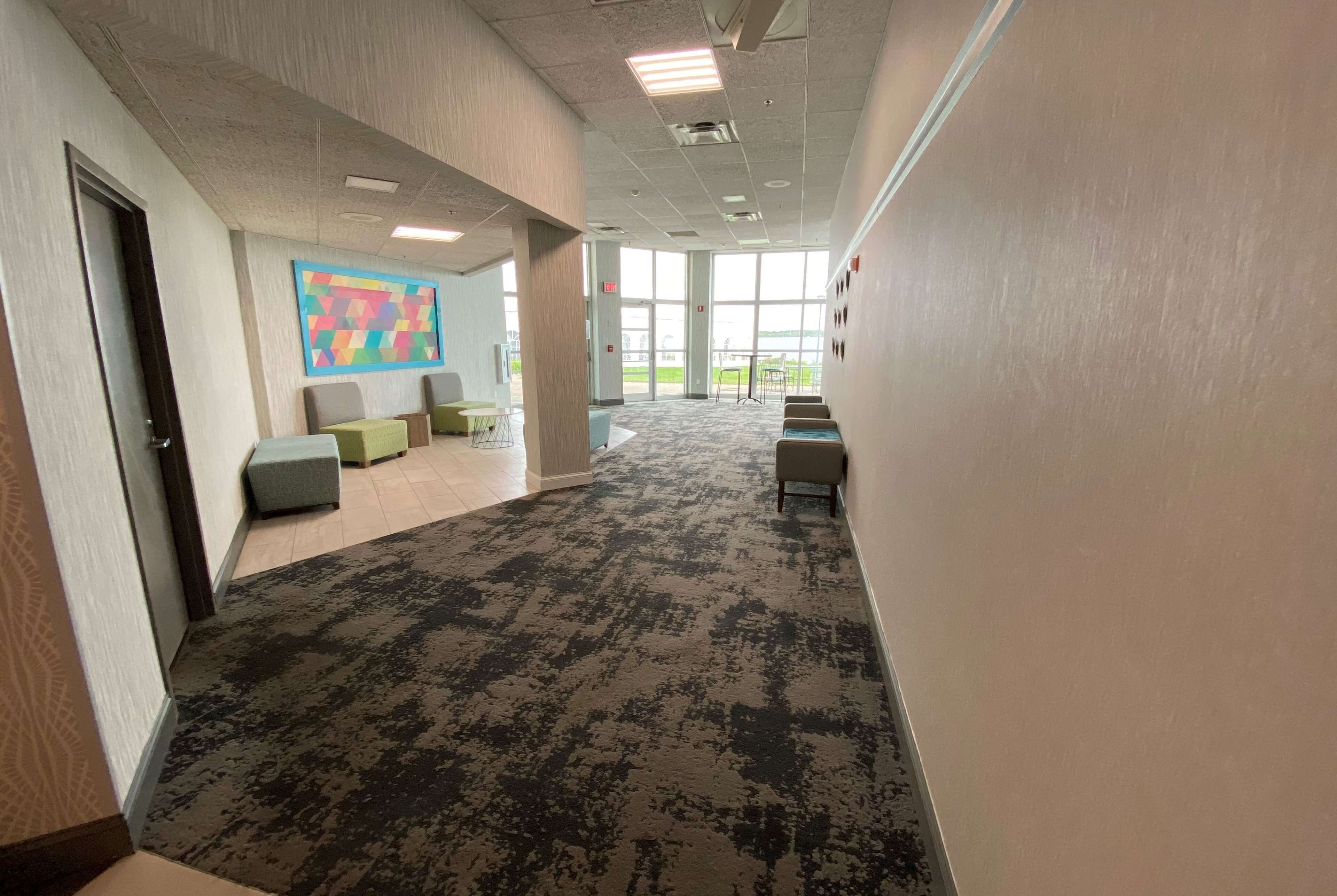 A spacious hallway with a patterned carpet, seating areas with cushions, and a large window providing natural light.