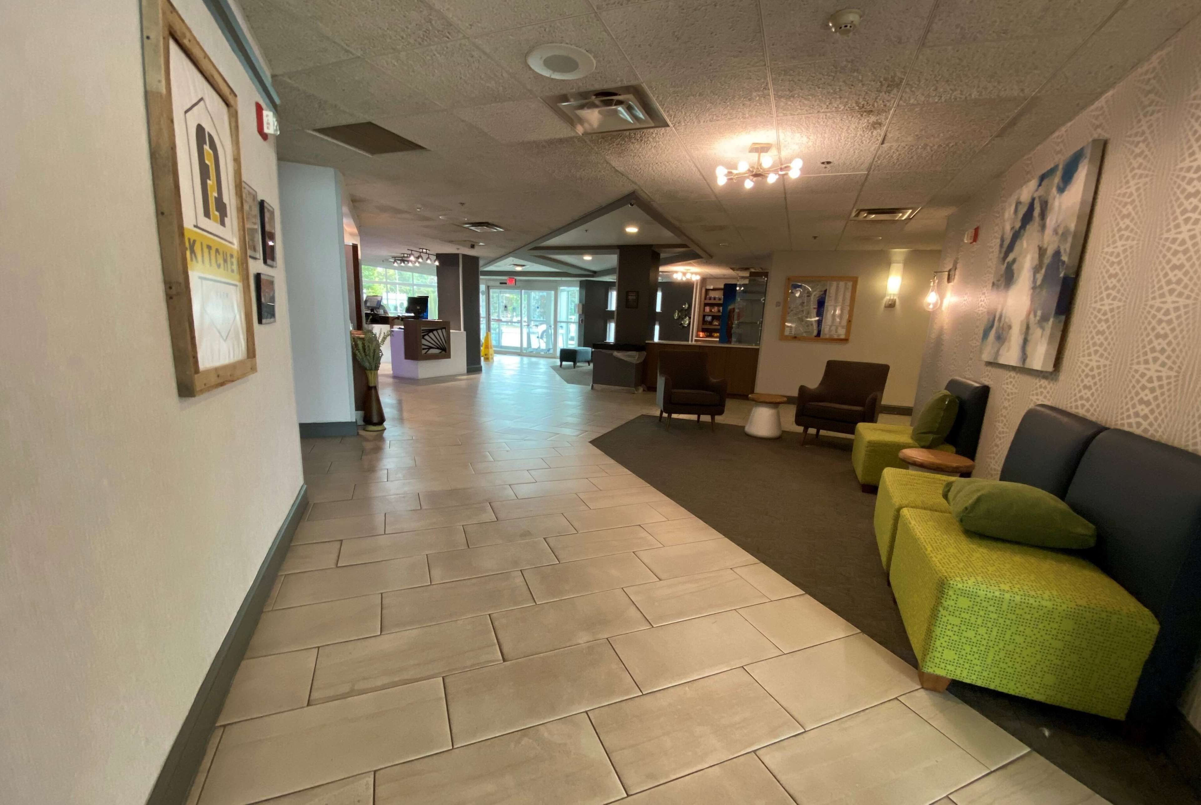 A hotel lobby with a herringbone floor pattern, a reception desk, seating area with green and brown upholstered chairs, and a large abstract painting on the wall.