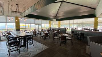 A spacious indoor area with multiple tables and chairs, large windows offering a view of the outdoors, and a ceiling with a unique geometric design.