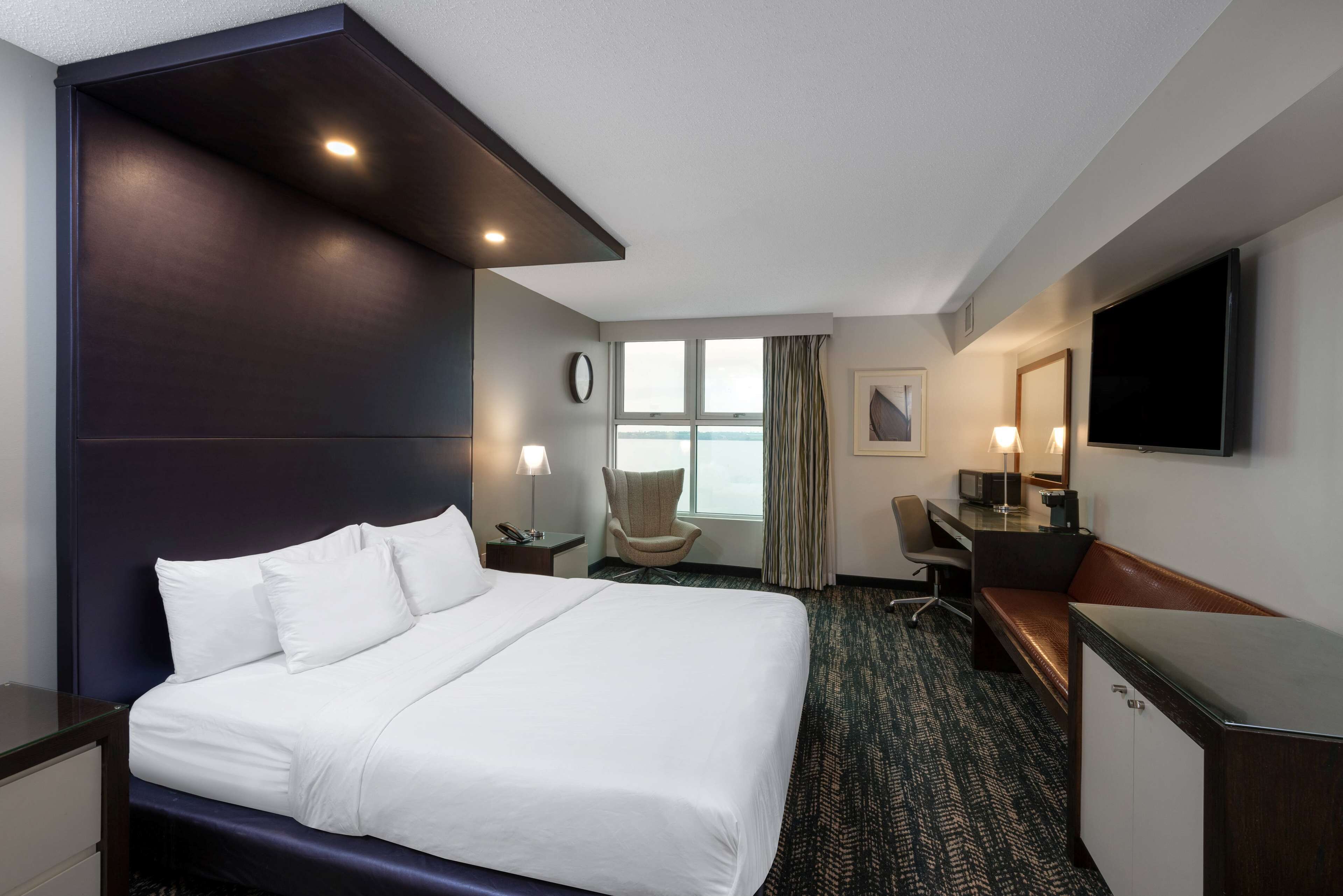 A hotel room with a large bed, a desk, a chair, a television, and a window with curtains.