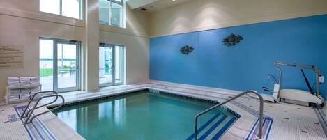 Una piscina interior con paredes de vidrio transparente, pared de azulejos azules y suelo de azulejos con una escalera de piscina.
