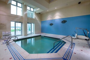 Piscina interior com paredes de vidro transparente, parede com azulejos azuis e chão revestido com uma escada para piscina.