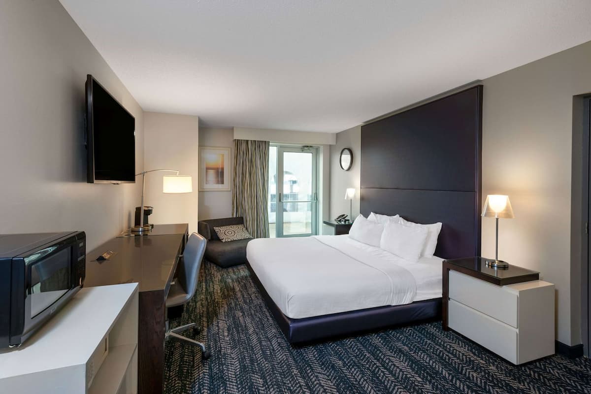 Ein Hotelzimmer mit Bett, Schreibtisch, Stuhl, Fernseher und Blick ins Freie.