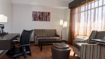 Habitación de hotel con escritorio, silla de oficina, sofá, otoman, sillón a rayas y un cuadro en la pared.