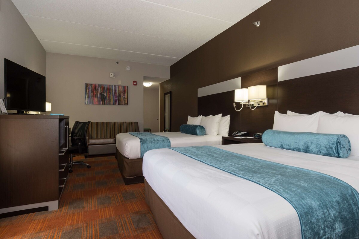 Una habitación de hotel con dos camas, un escritorio, un televisor y un cuadro en la pared.