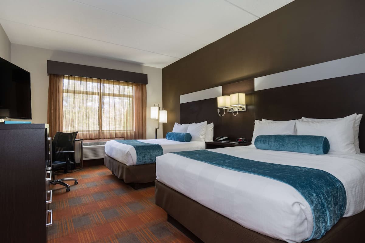 Een hotelkamer met twee bedden, een bureau, een stoel, een televisie en een raam met gordijnen.