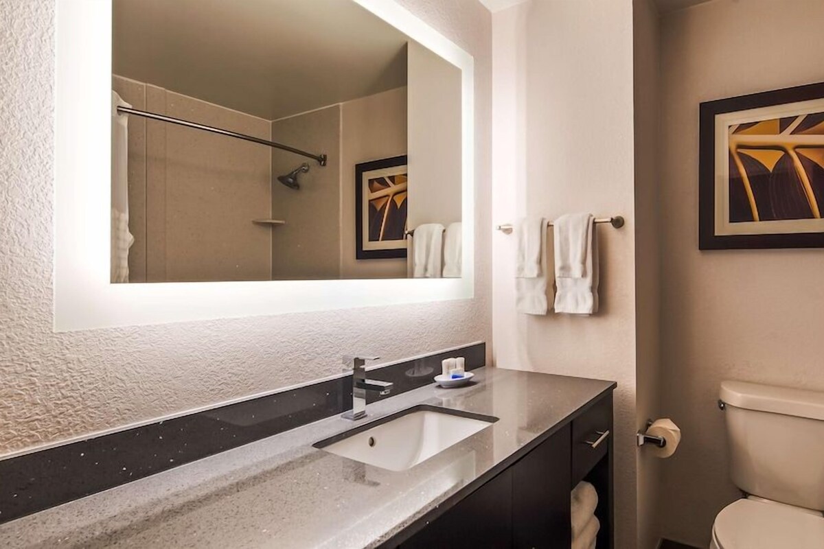 Une salle de bain équipée d’un lavabo, d’un miroir, d’un porte-serviettes, de toilettes et d’un tableau encadré au mur.