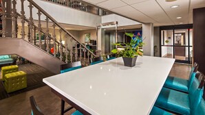Un hall d’entrée spacieux avec un comptoir de réception blanc, un escalier orné de rampes en métal ouvragé et un coin salon avec des chaises bleues et jaunes.