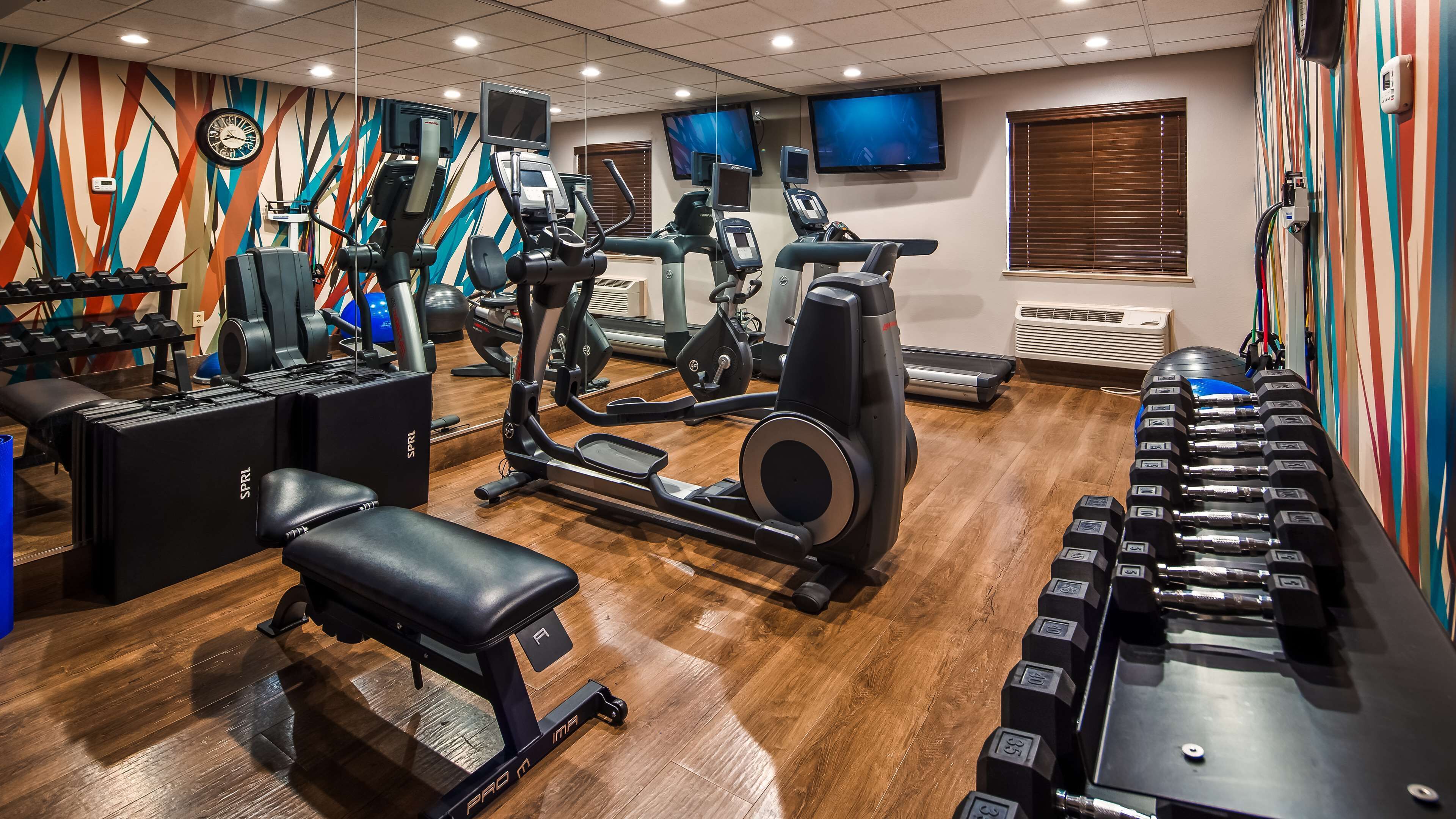 A gym with various exercise equipment, including treadmills, an elliptical, and dumbbells.