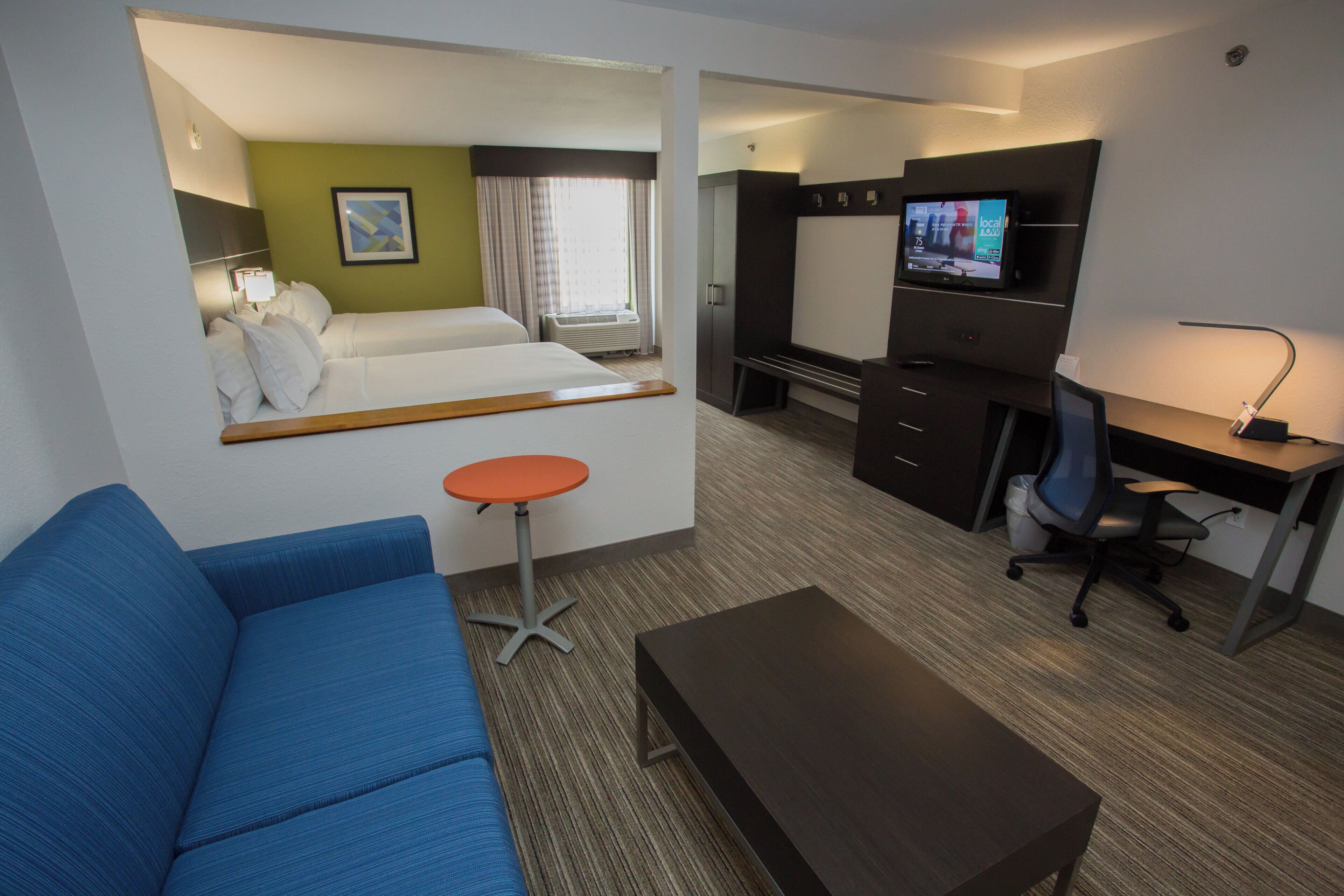 A hotel room with a bed, a desk, a chair, a small table, and a television.