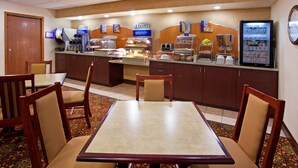A breakfast area with a counter, coffee machines, and a yogurt dispenser. There are wooden chairs and a table with a patterned table runner. - Holiday Inn Express Wilmington by IHG (Wilmington)
