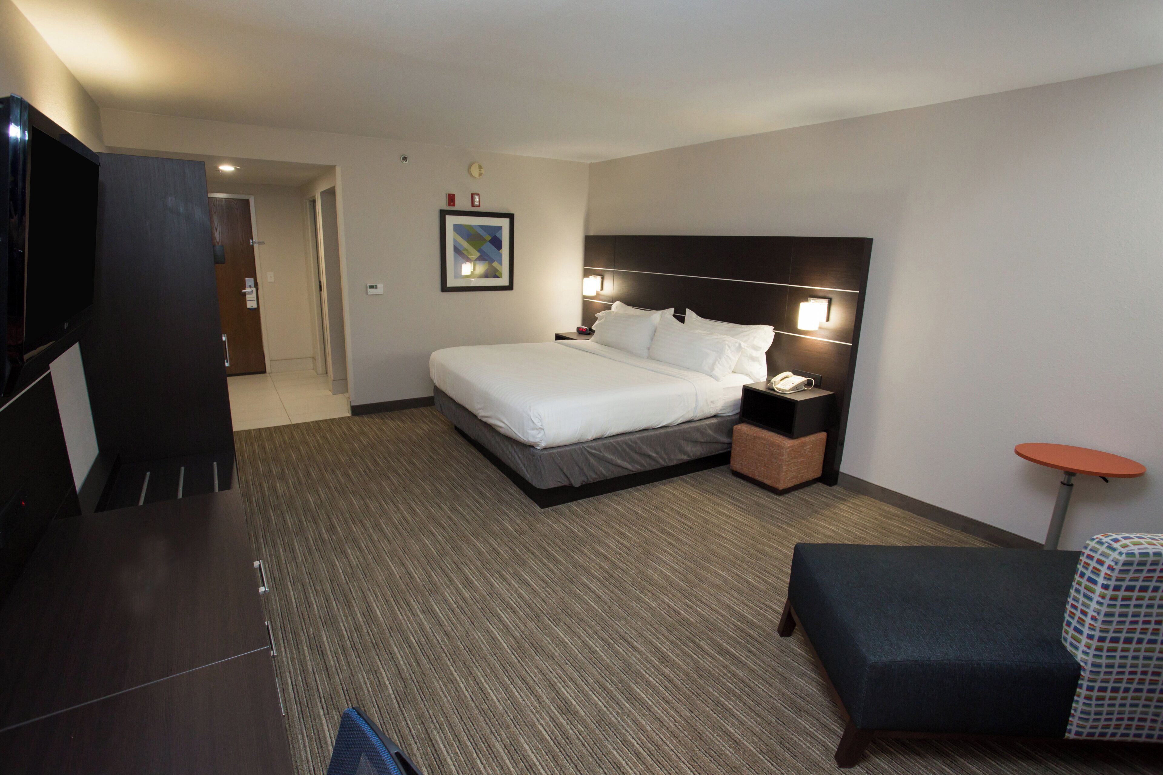A hotel room with a bed, bedside table, lamp, TV, and a small round table.