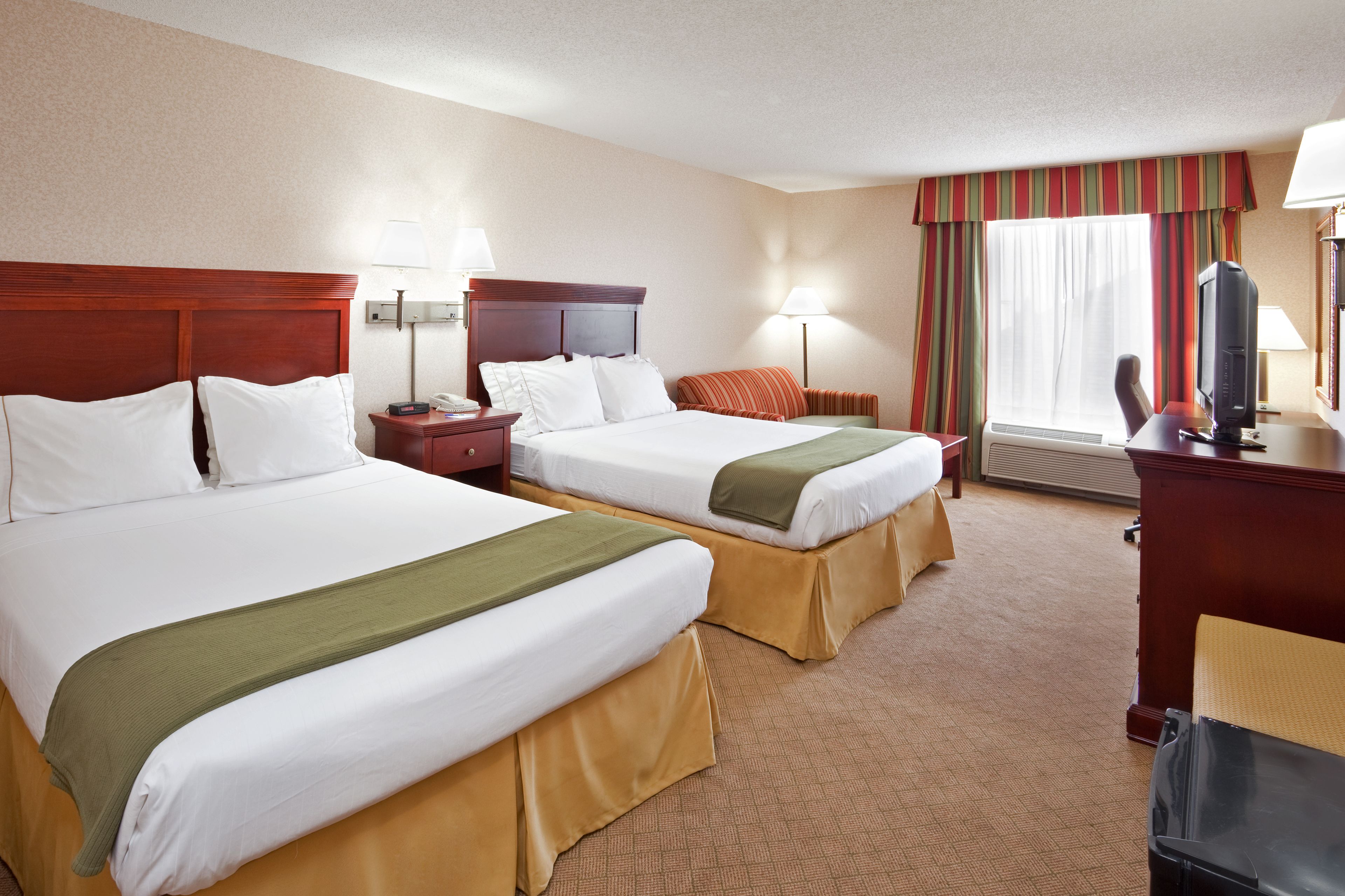 A hotel room with two beds, a desk, a chair, a television, and a window with curtains.