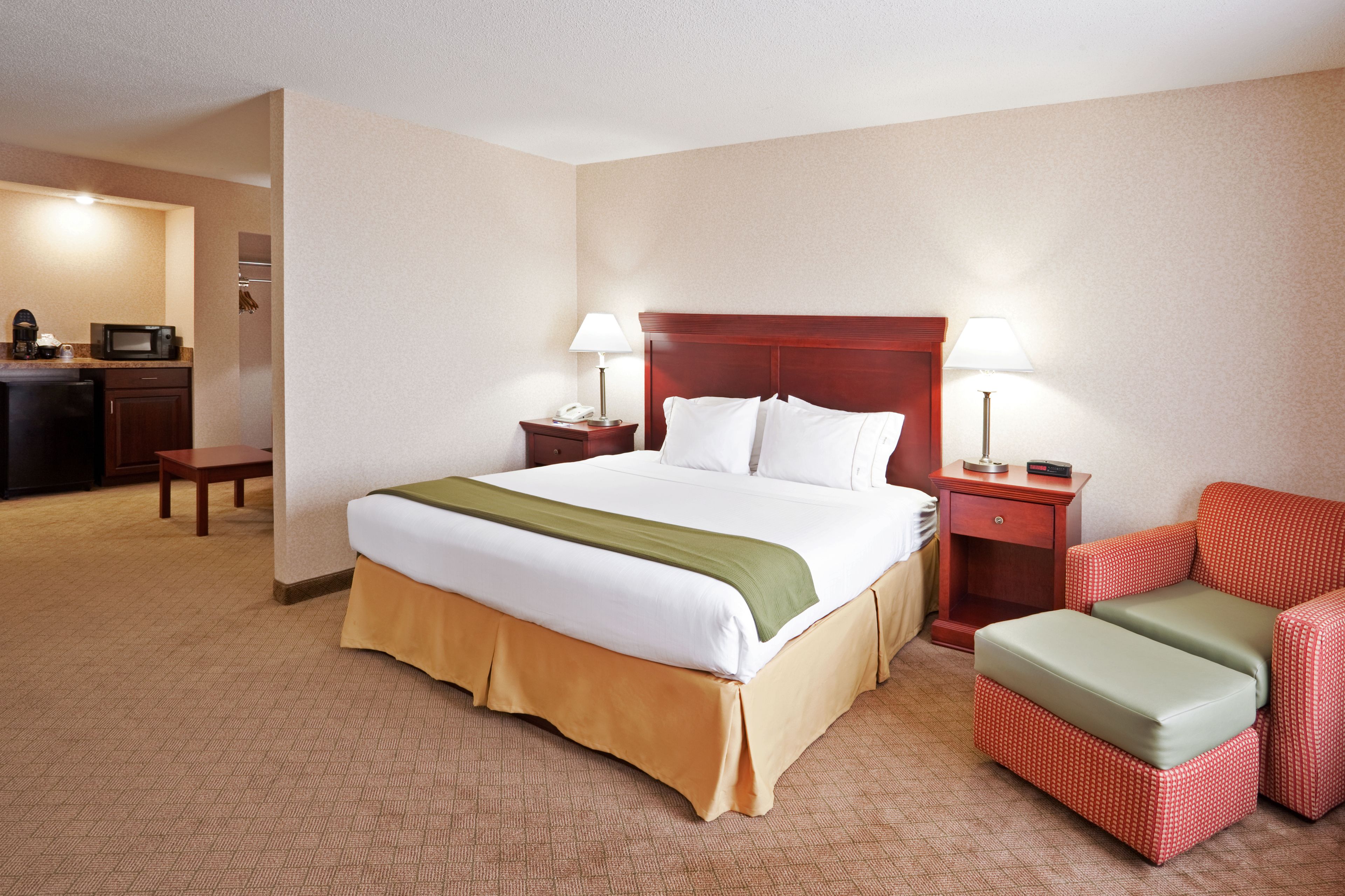 Une chambre d’hôtel avec un grand lit, deux tables de chevet, un fauteuil rouge, un petit bureau avec une lampe et un four à micro-ondes.