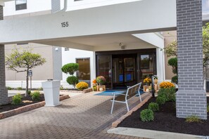 A building entrance with a covered walkway, numbered 155, and a bench outside.