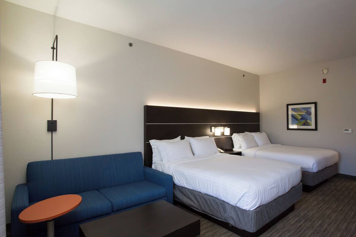 Hotellihuone, jossa on kaksi sänkyä, sohva, pieni pöytä ja lamppu.