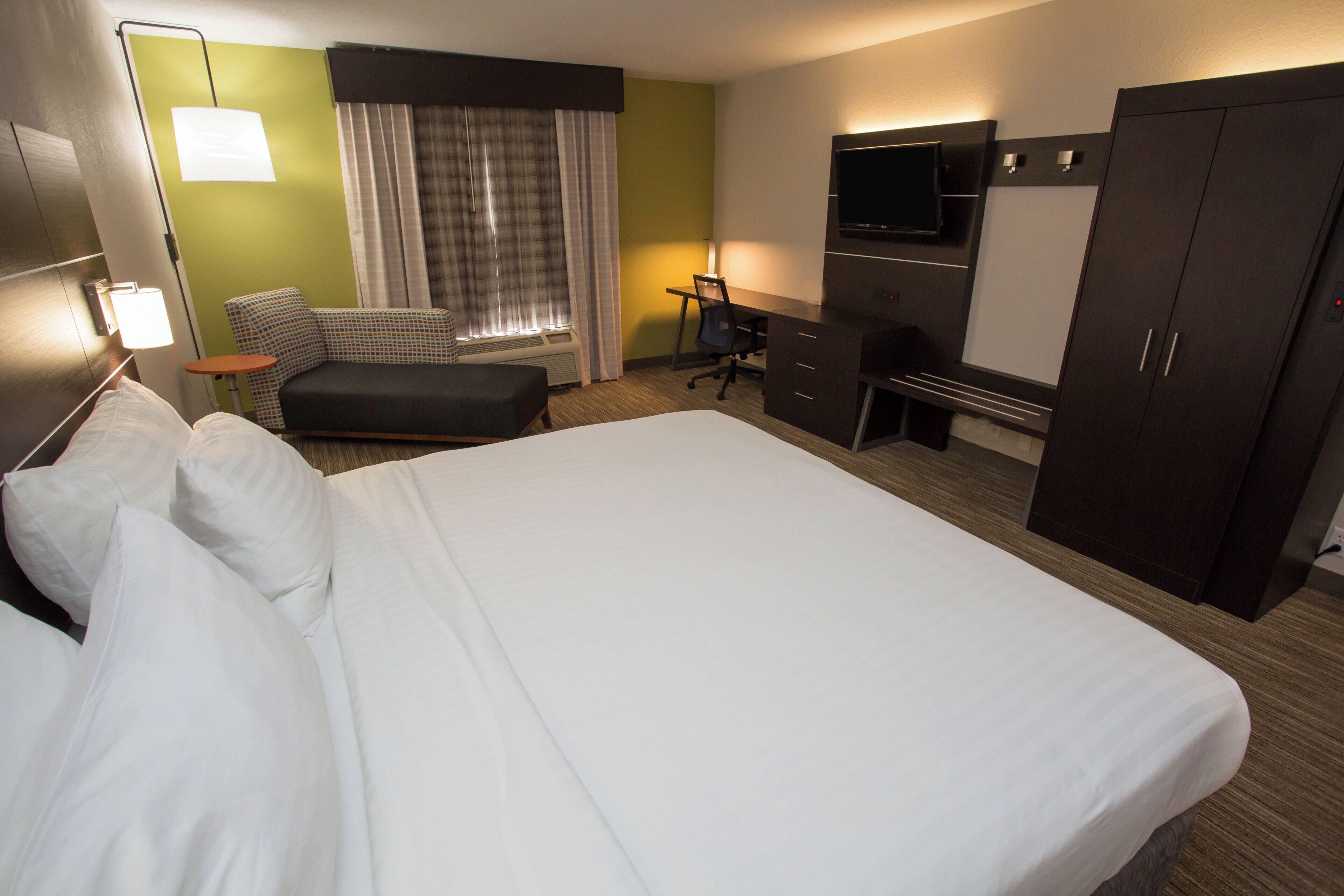 A hotel room with a large bed, a desk, a chair, a TV, and a wardrobe.