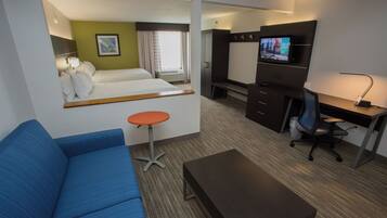 A hotel room with a bed, a blue sofa, a desk with a computer, a TV, and a small table.