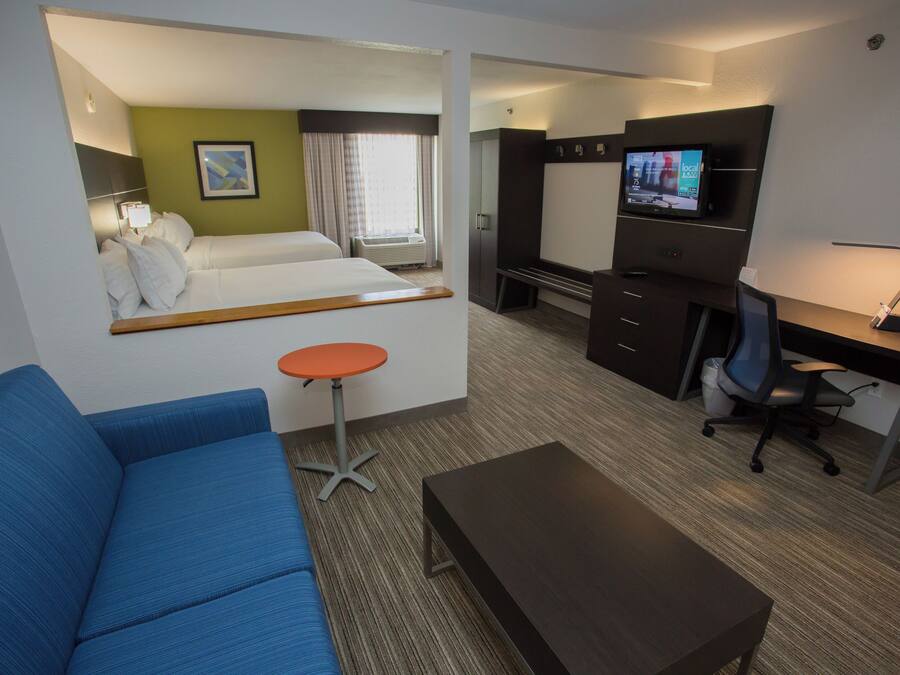 A hotel room with a bed, a blue sofa, a desk with a computer, a TV, and a small table.