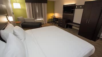 A hotel room with a large bed, a desk, a chair, a TV, and a wardrobe.