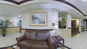 A lobby with a brown leather sofa, a framed landscape painting, and a small table with a lamp. - Holiday Inn Express Wilmington by IHG (Wilmington)