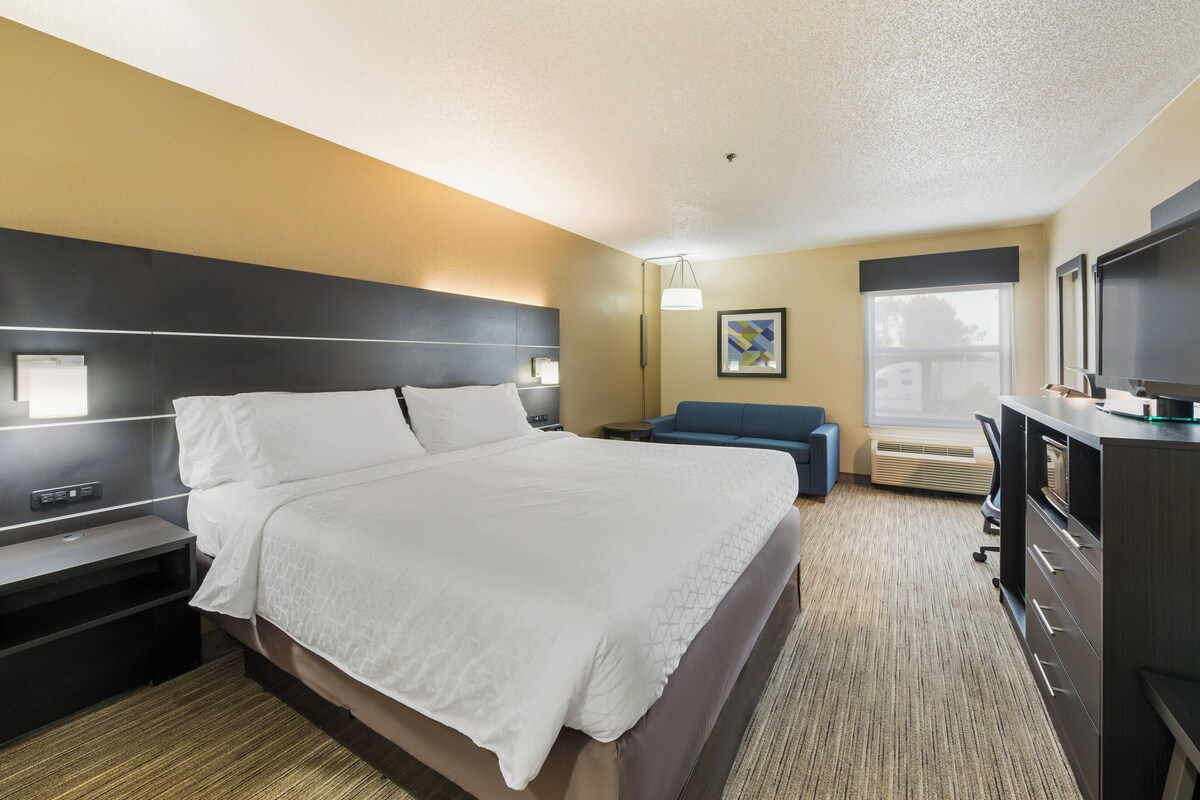 A hotel room with a large bed, bedside tables, a desk with a flat-screen TV, a blue sofa, and a painting on the wall.