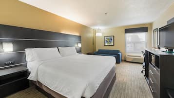 A hotel room with a large bed, bedside tables, a desk with a flat-screen TV, a blue sofa, and a painting on the wall.
