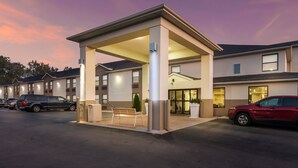 A hotel with a covered outdoor seating area, multiple parking spaces, and a well-lit entrance.