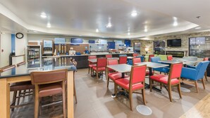 Un restaurant moderne doté d’un bar, de sièges rouges et bleus et d’un téléviseur à écran plat fixé au mur.
