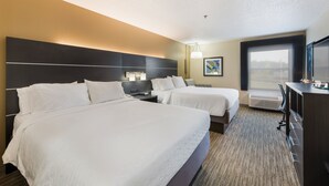 A hotel room with two beds, a desk, a dresser, and a large window.