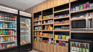 A self-service beverage and snack area with refrigerated drink dispensers, shelves stocked with snacks, and a microwave. - Spark by Hilton Lancaster (Lancaster)