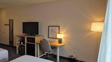 A hotel room with a bed, a desk with a chair, a television, a lamp, and a trash bin.