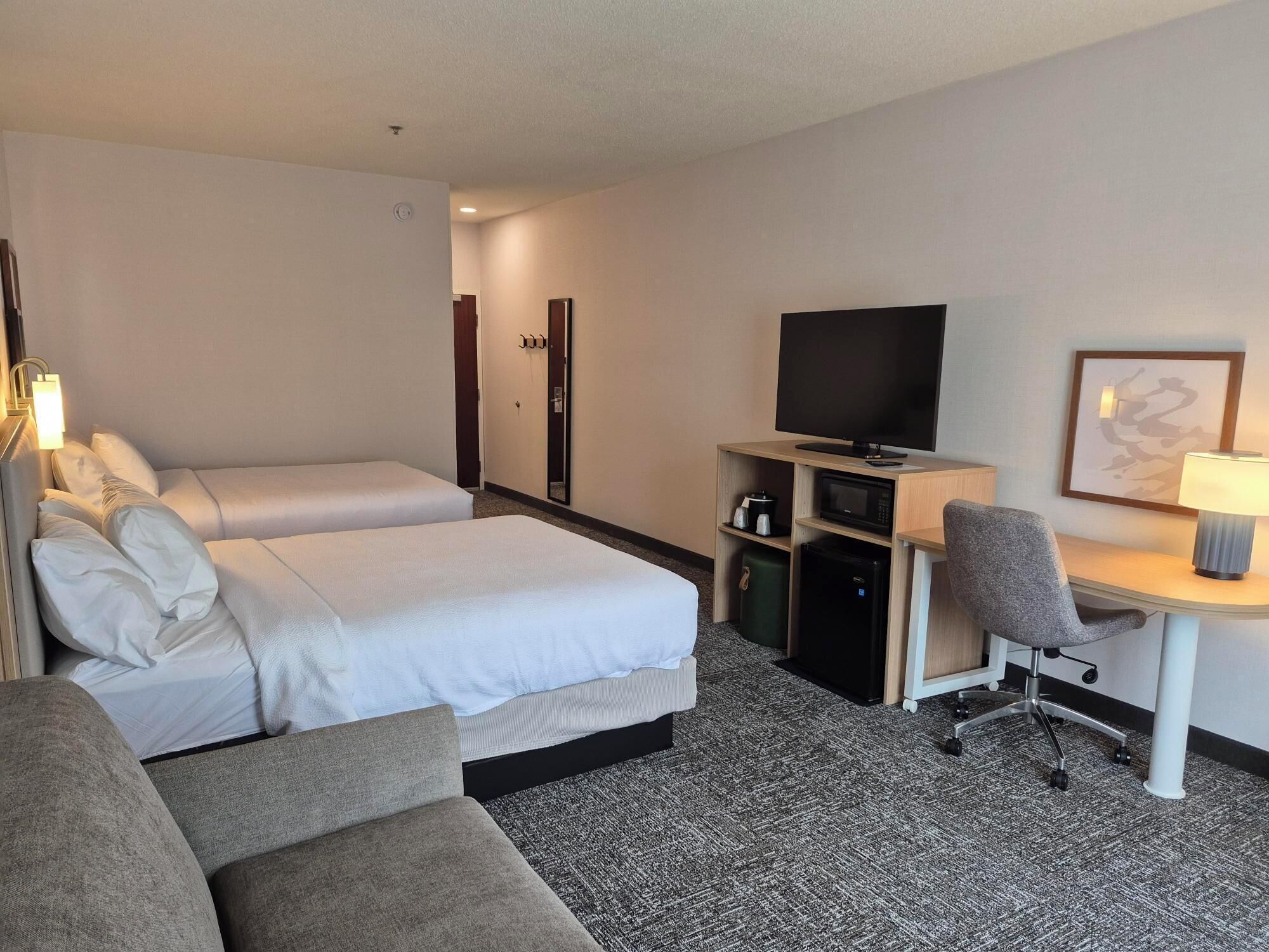 A hotel room with two beds, a desk with a TV, a chair, and a microwave.