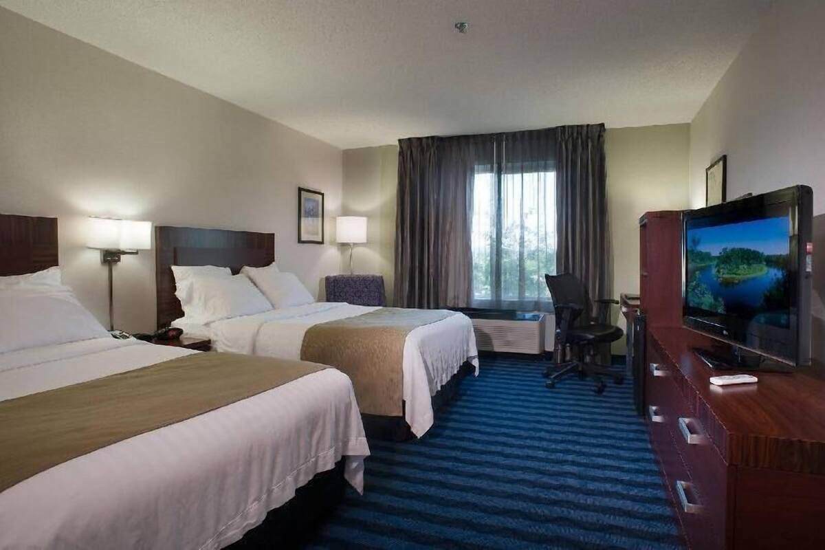 A hotel room with two beds, a TV, a desk, and a window with curtains.