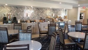 A restaurant with a herringbone-patterned wall, a buffet area with food displays, and a seating area with round tables and upholstered chairs. - Spark by Hilton Lancaster (Lancaster)