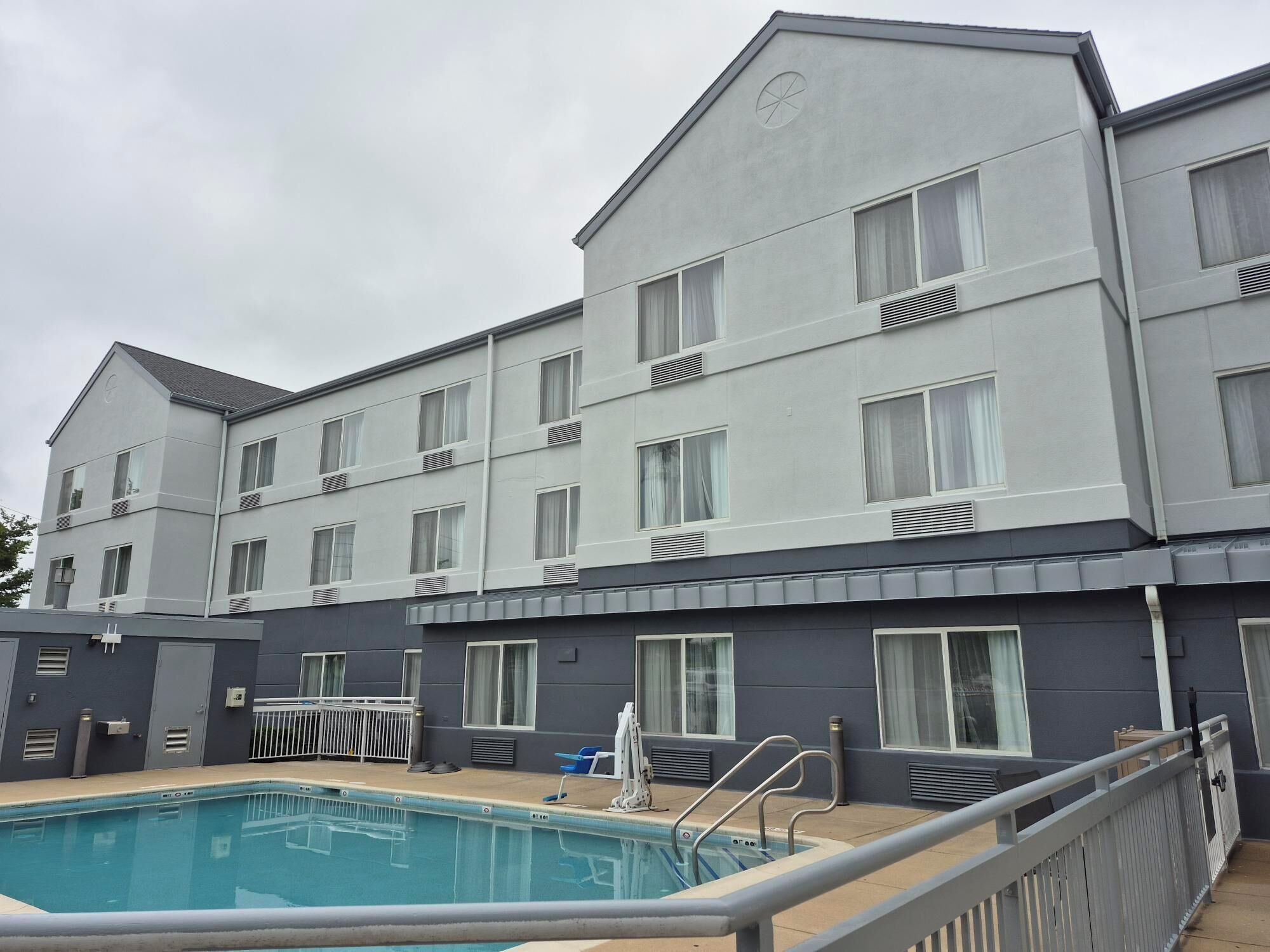 A modern hotel with a swimming pool, multiple balconies, and a grey facade.