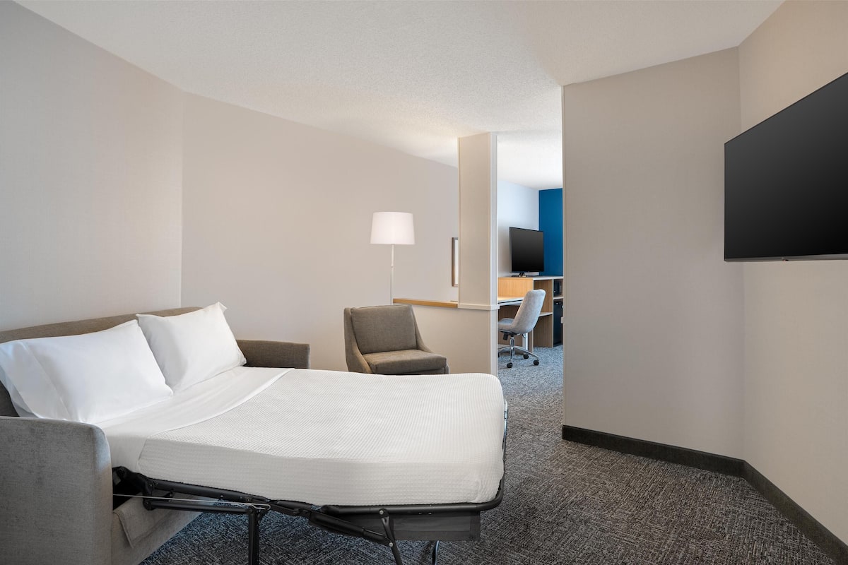 A hotel room with a bed, a chair, a desk, a TV, and a lamp.