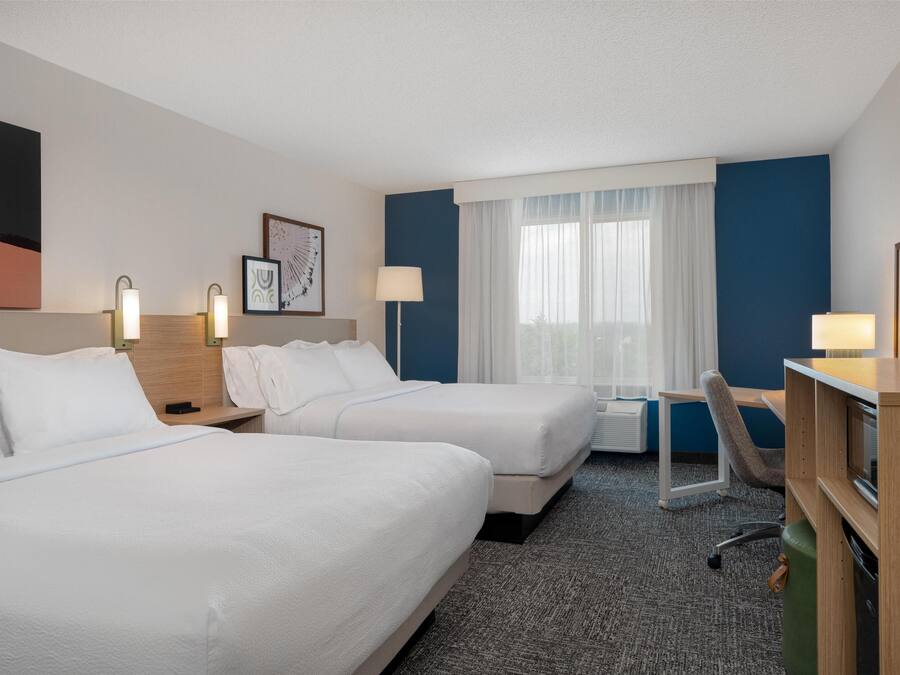 A hotel room with two beds, a desk, a chair, and a TV.