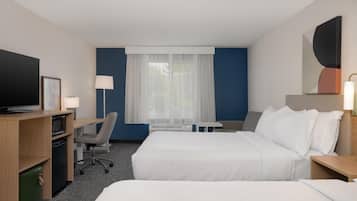 A hotel room with two beds, a desk with a computer, a TV, and a window with curtains.