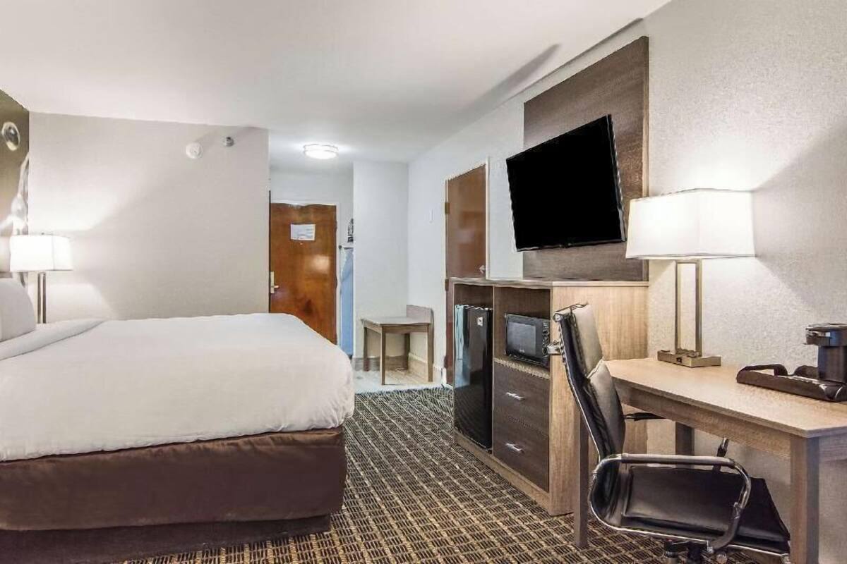 Una habitación de hotel con cama, escritorio, silla, televisor y una mesita.