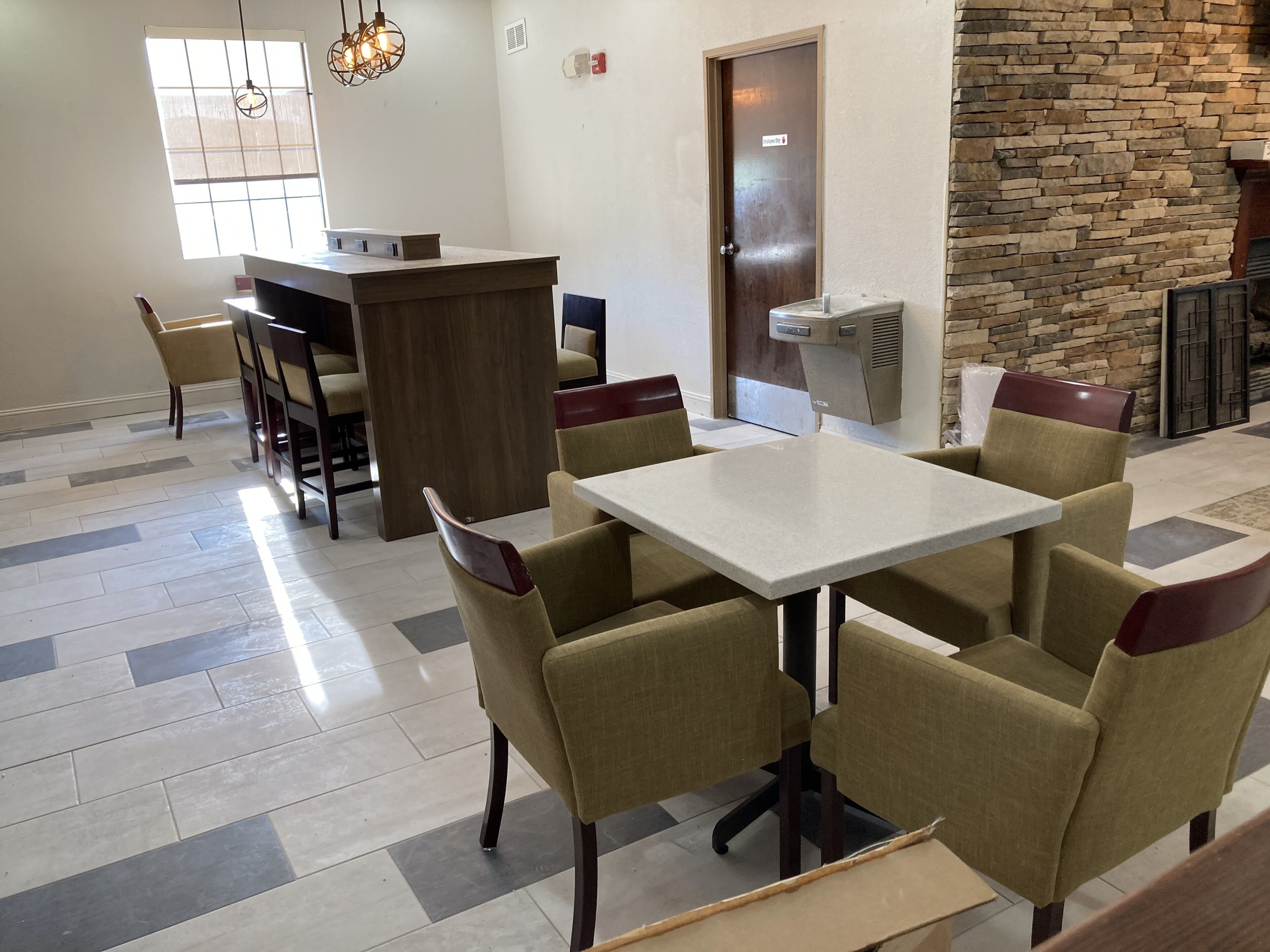 A dining area with a square table and six chairs, a reception desk, and a stone wall.