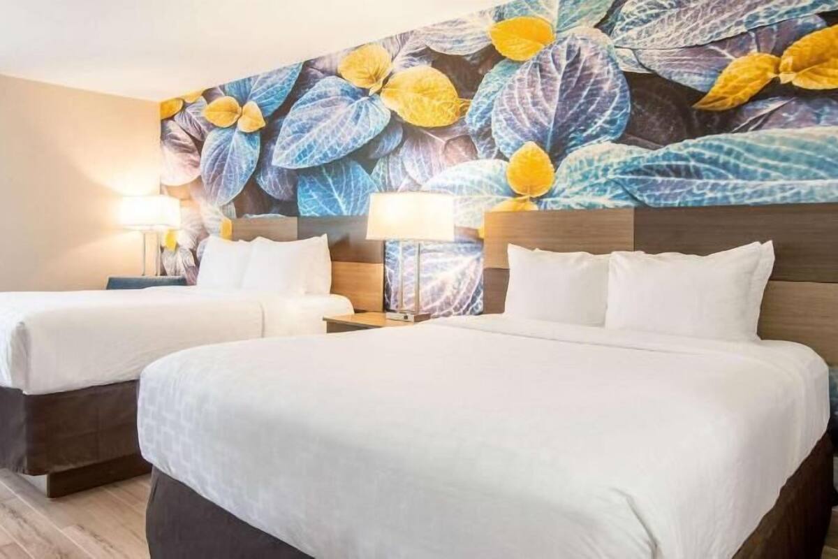 Una habitación de hotel con dos camas, un gran mural floral en la pared y lámparas de noche.