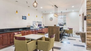 Une cuisine moderne avec des meubles en bois, un plan de travail blanc et des luminaires suspendus. On y trouve également un coin repas avec des chaises et une table.